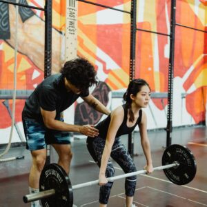 A young woman lifting a barbell in a gym with a trainer's guidance. Perfect for fitness and training themes.