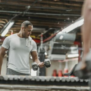 Adult man working out with dumbbells, reflecting in the gym mirror, showcasing strength and determination.