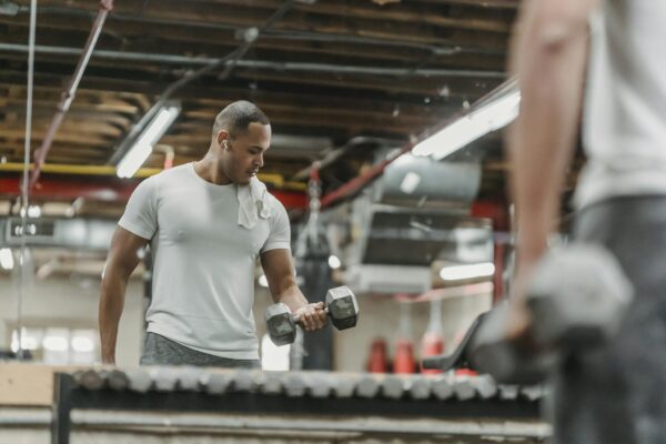 Adult man working out with dumbbells, reflecting in the gym mirror, showcasing strength and determination.
