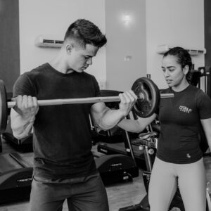 Male athlete lifting weights with female trainer guidance in modern gym.